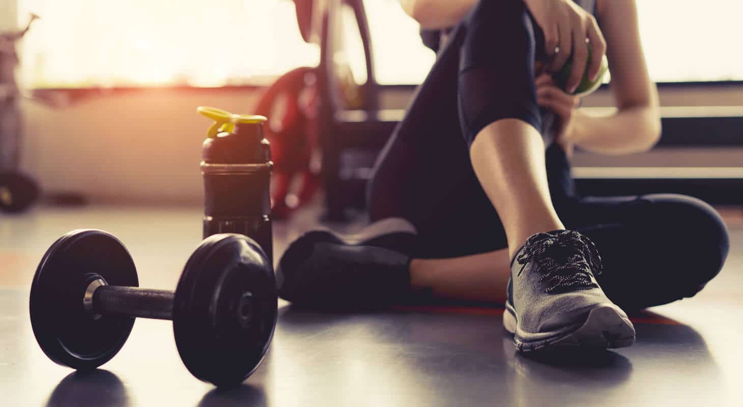 Woman resting next to sports bottle and dumbbell in gym
