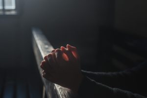 Hands folded into prayer in a church pew.