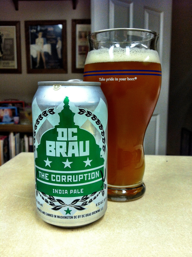 Silver and green can of DC Brau Beer with glass filled with dark golden beer. 