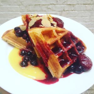 Golden waffles with fruit syrup dripping in colorful display served on white plate