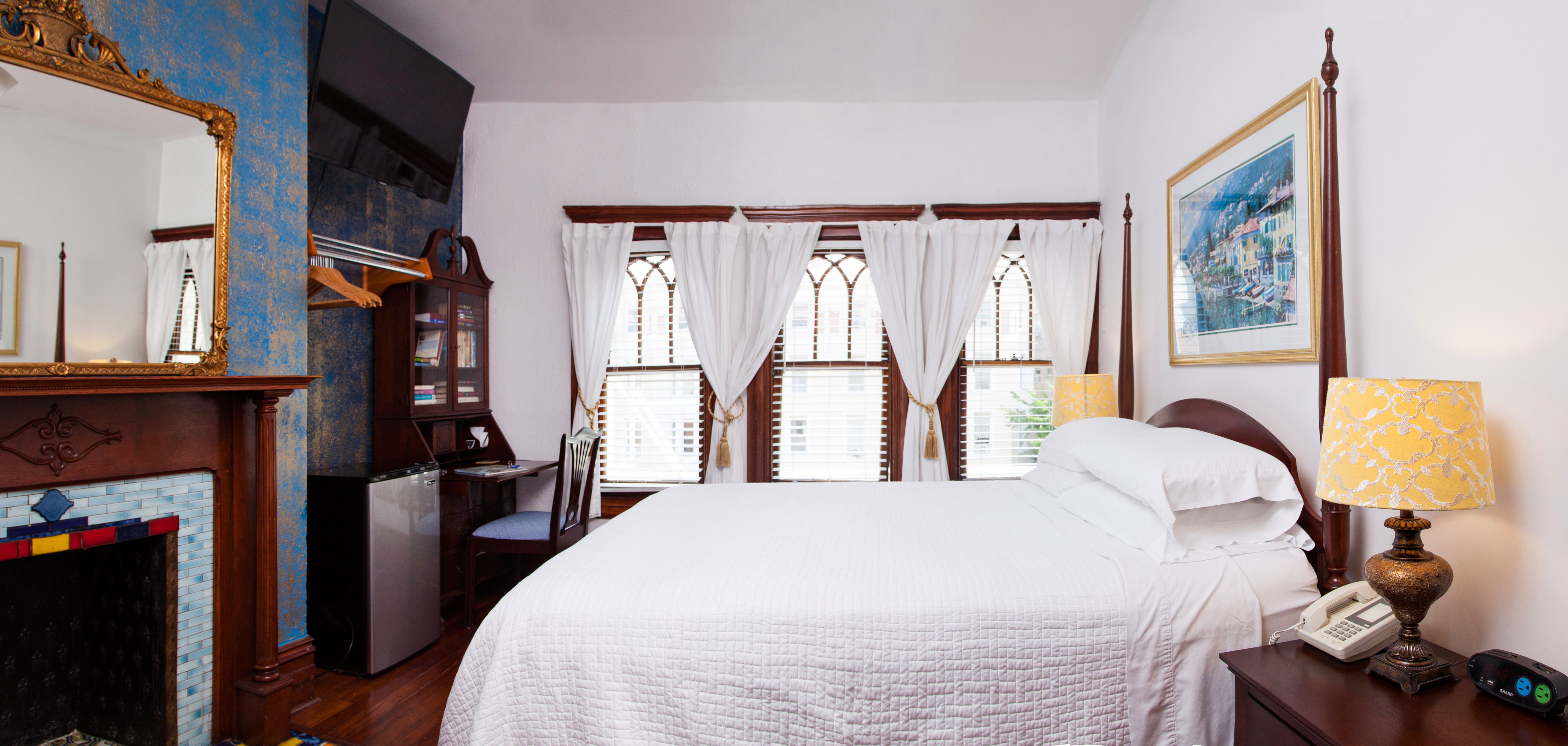 Clean and attractive guestroom with blue and white walls and ornate fireplace; featuring neatly made bed in white bedding
